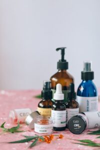 Assorted CBD and hemp products including oil drops, capsules, pain relief salve, face serum, and hemp lotion on pink surface.