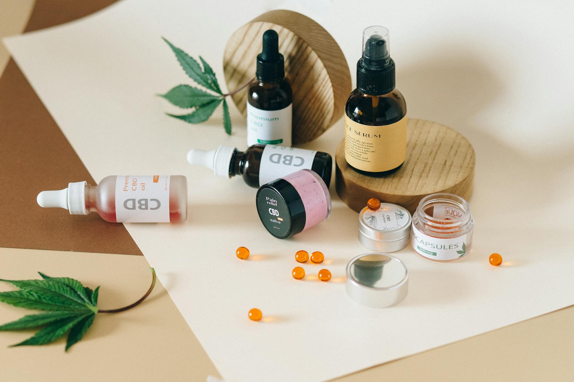 Assorted CBD products including tincture oils, face serum, pain relief salve, capsules, and gel beads on a beige surface with